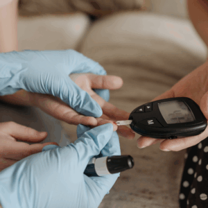 a pair of nitrile gloved hands assisting another set of hands in testing their blood sugar with a handheld glucometer