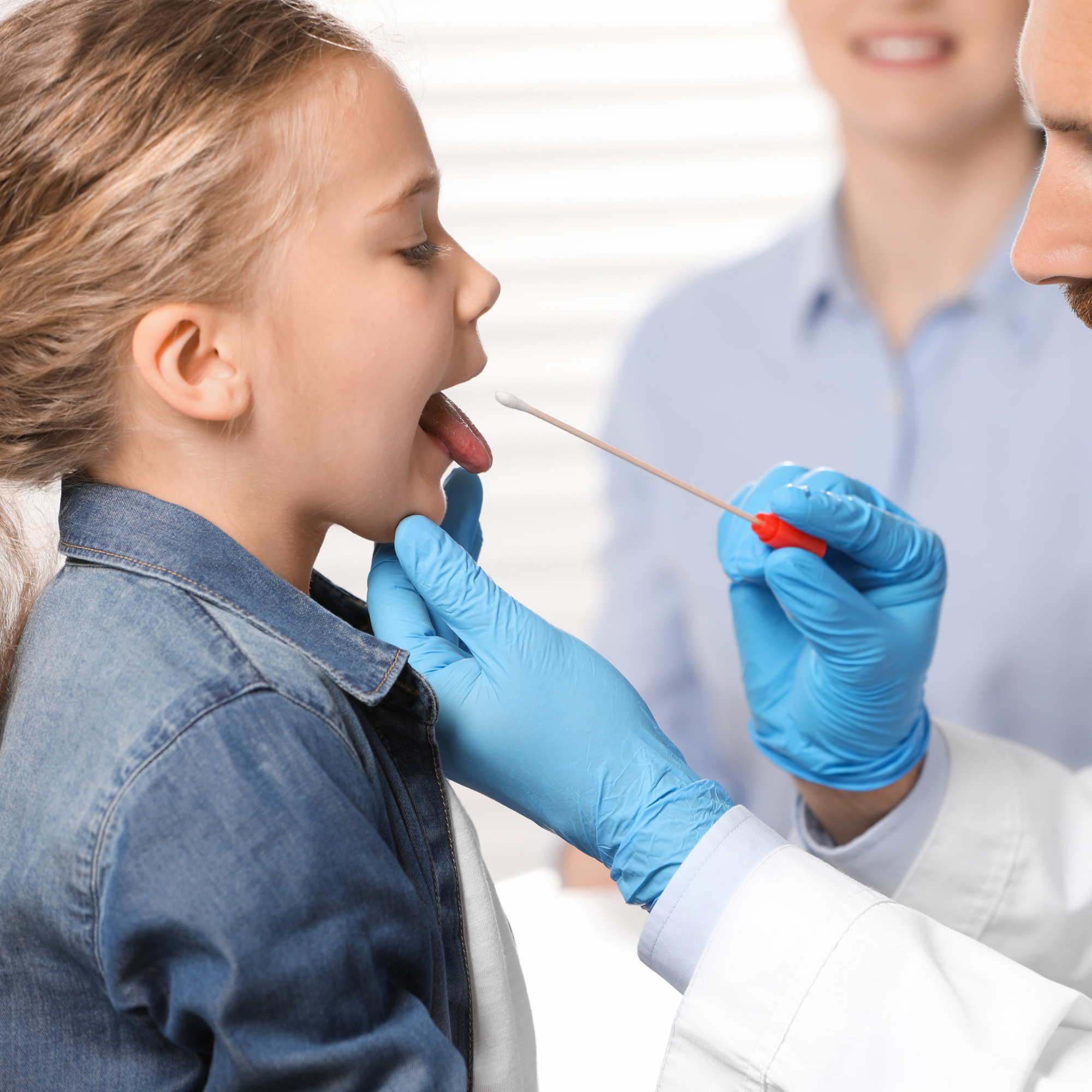 A youn girl undergoing a throat swab by a man in blue nitrile gloves.